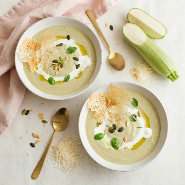 Dos platos de crema de zapallo italiano con parmesano y albahaca, vistos desde arriba.